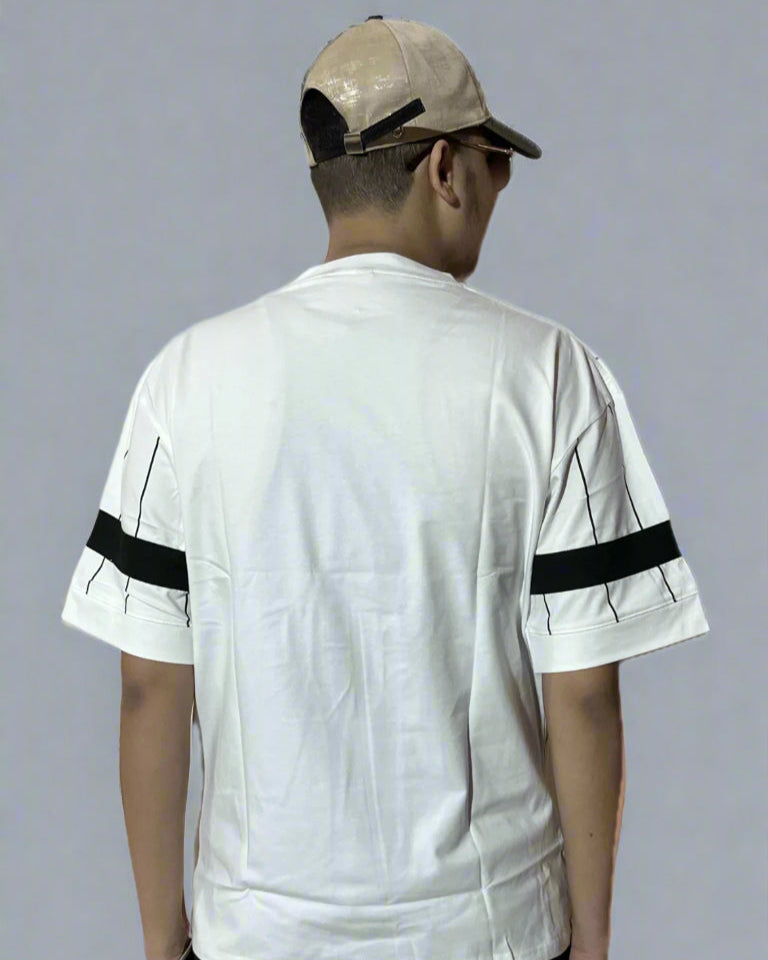 Person wearing a white t-shirt with black stripes on sleeves and a beige cap, standing against a gray background