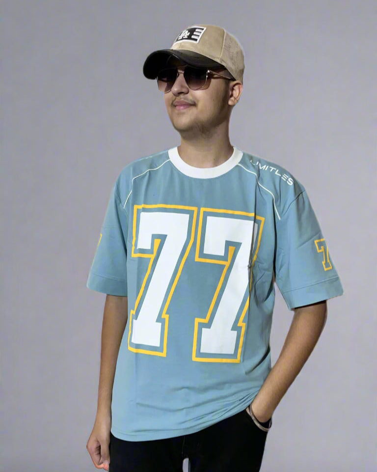 Person wearing a light blue sports jersey with the number 77, black pants, and a beige cap on a light gray background.