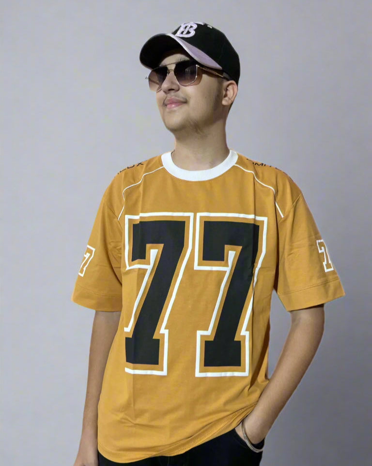 Person wearing a mustard yellow sports jersey with the number 77, black cap, and sunglasses on a light blue background