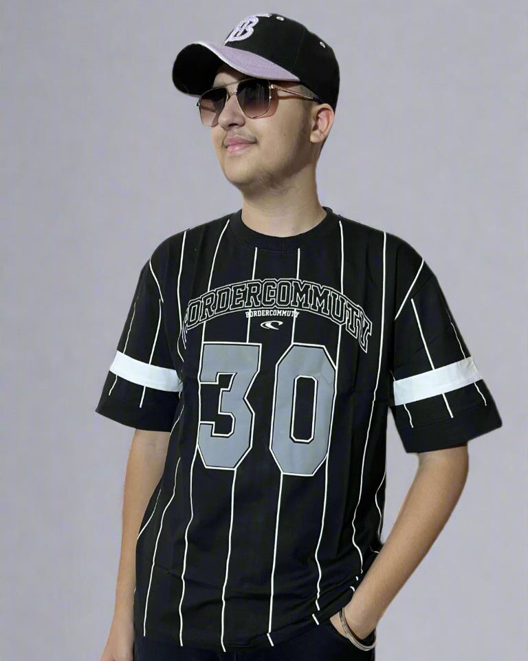 Person wearing a black sports jersey with white stripes and a cap on a plain background