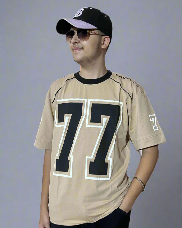 Person wearing a beige sports jersey with the number 77, black cap, and sunglasses on a light gray background