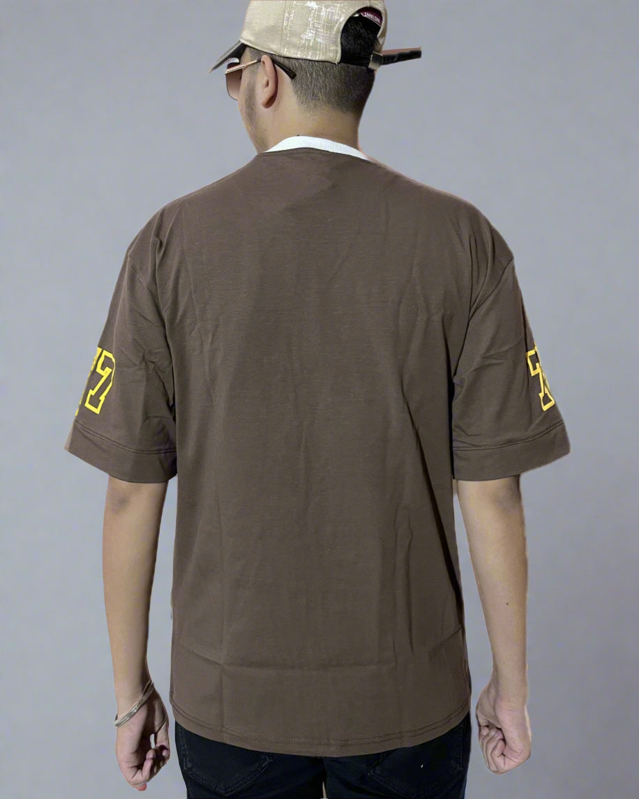Person wearing a brown shirt with yellow logos on the back, standing against a light gray background