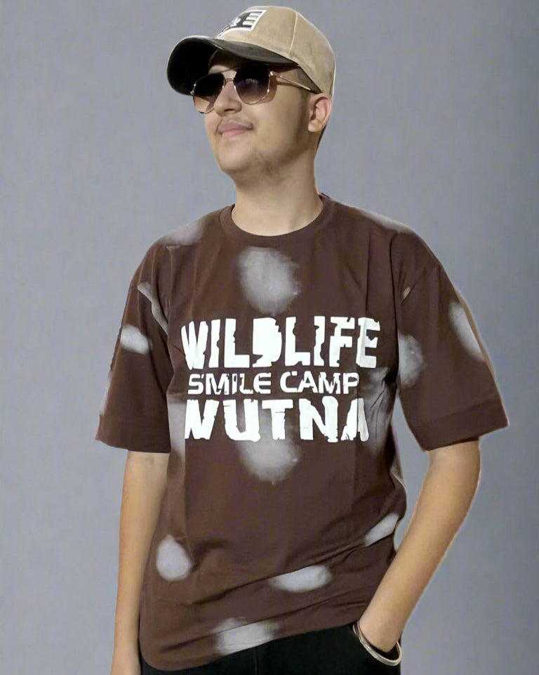 Person wearing a brown t-shirt with text and a cap, standing against a gray background