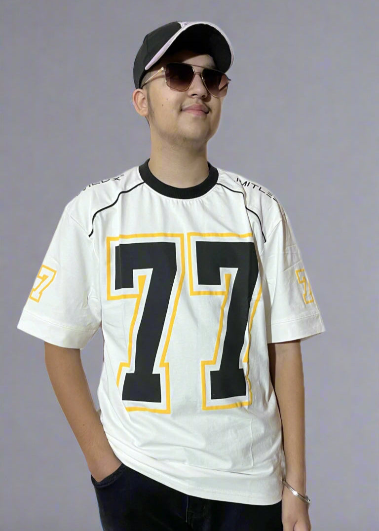 Person wearing a white sports jersey with the number 77, black pants, and a cap on a light gray background