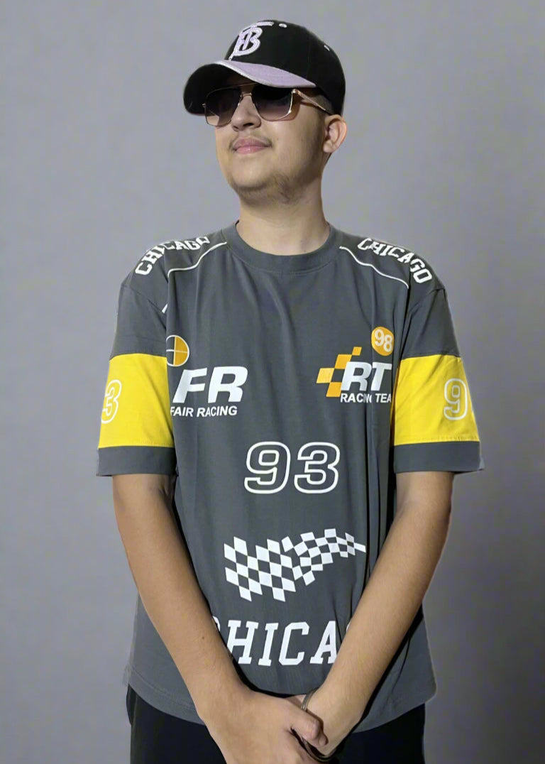 Person wearing a gray and yellow racing-themed shirt with visible branding on a light blue background
