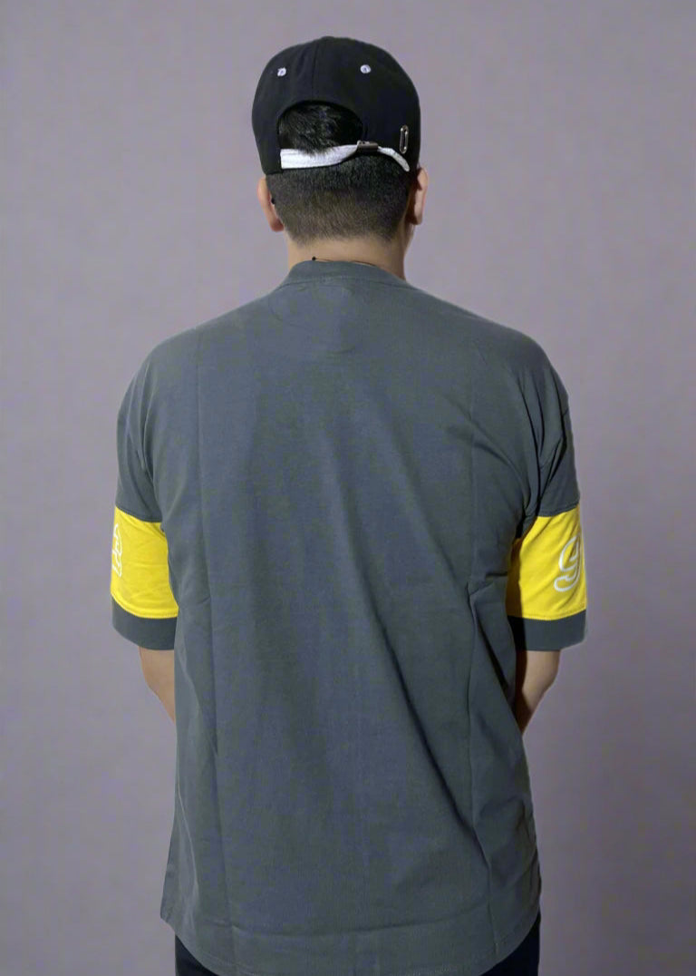 Person wearing a gray shirt with yellow sleeves and a black cap on a gray background