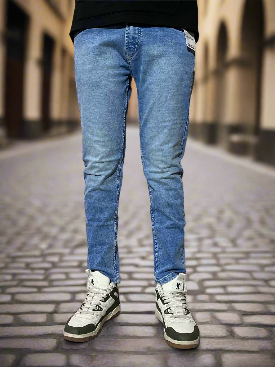 Person wearing blue jeans and white sneakers against a beige wall.