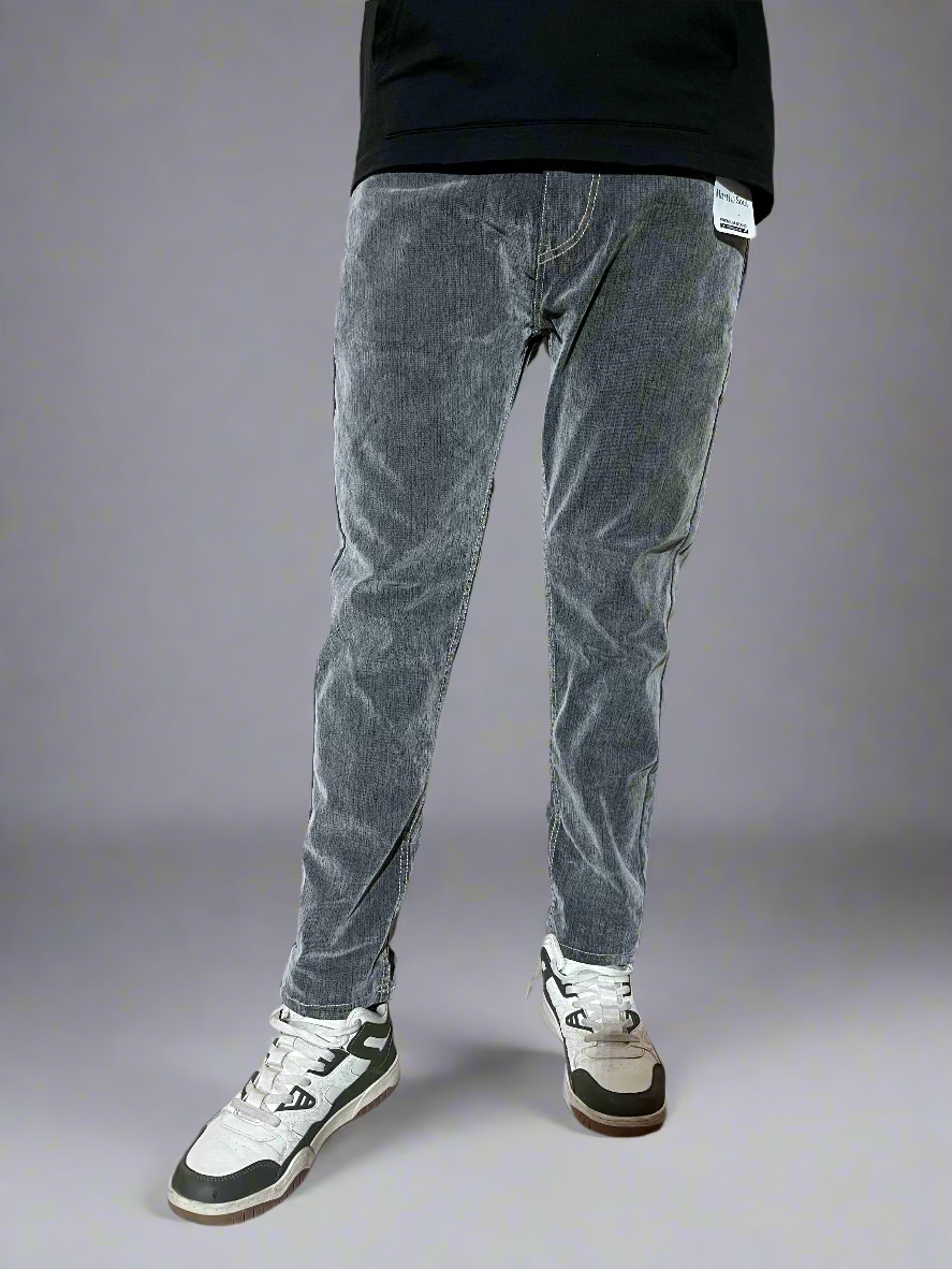Person wearing gray jeans and black and white sneakers against a plain background