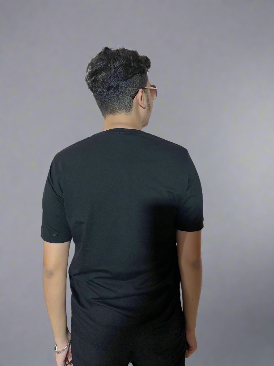 Person wearing a black t-shirt standing against a light-colored wall with decorative floral patterns.