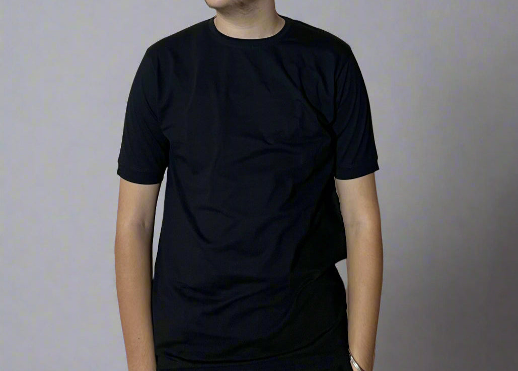 Person wearing a black t-shirt and sunglasses against a light-colored wall with text and symbols.